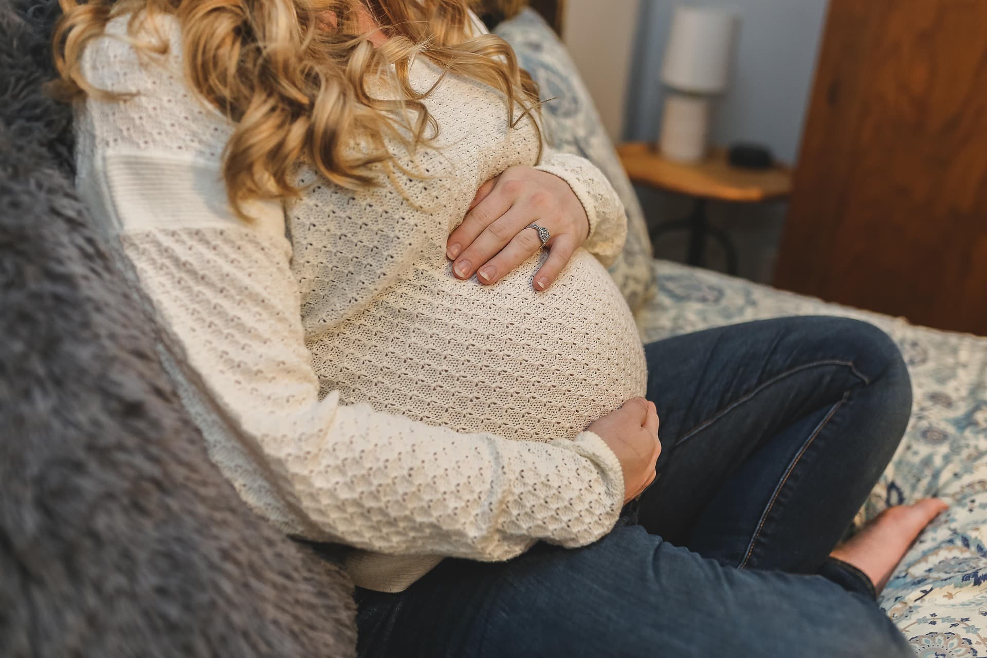 A pregnant woman sitting on a couch legs crossed holding her tummy